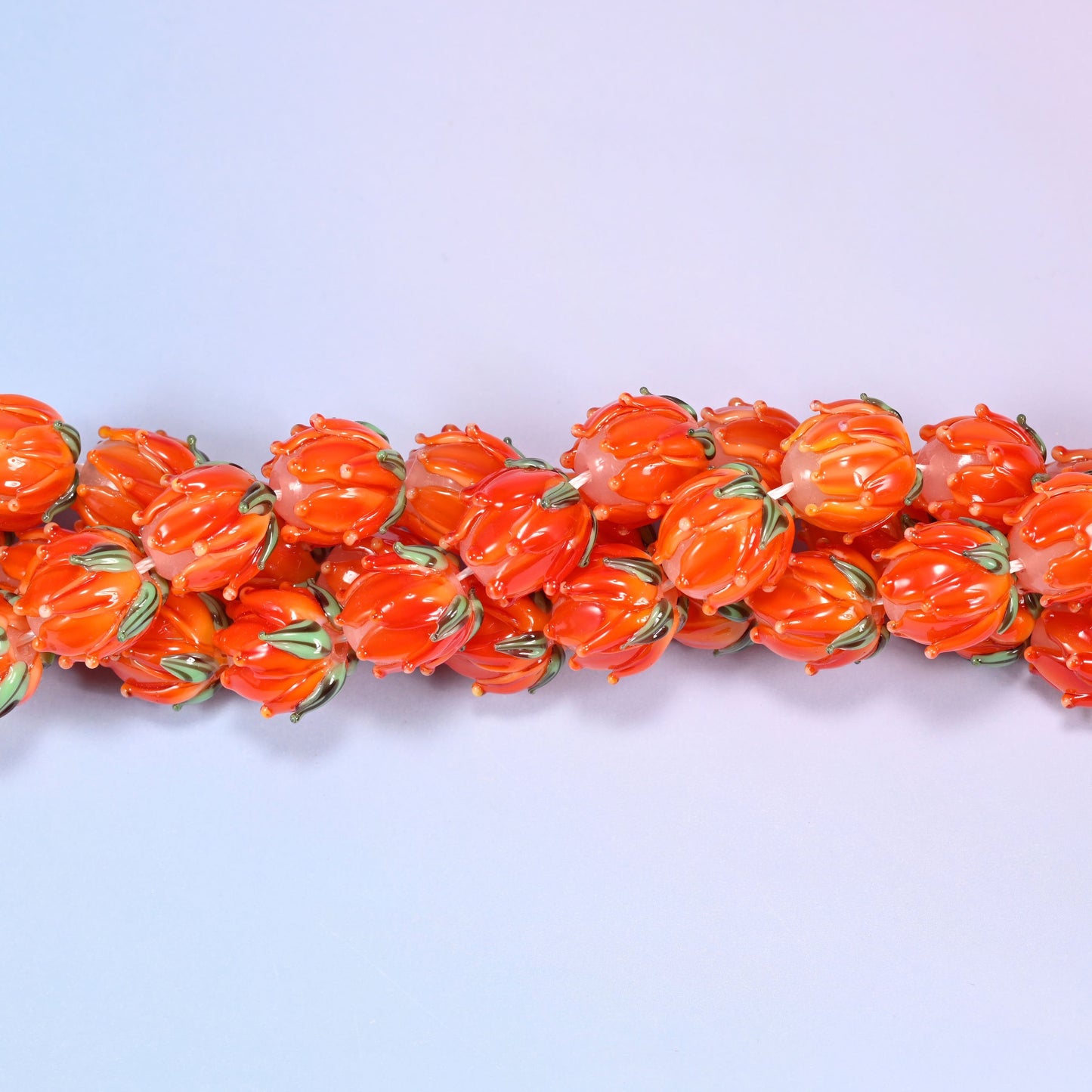 Orange tulip bud-shaped lampwork glass beads, hand-formed with sculpted petal detailing that gives a realistic flower bud look, accented with a green leaf detail at the base.