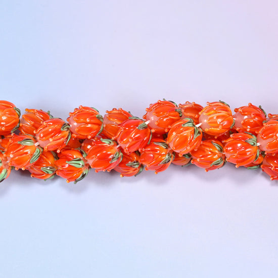 Orange tulip bud-shaped lampwork glass beads, hand-formed with sculpted petal detailing that gives a realistic flower bud look, accented with a green leaf detail at the base.