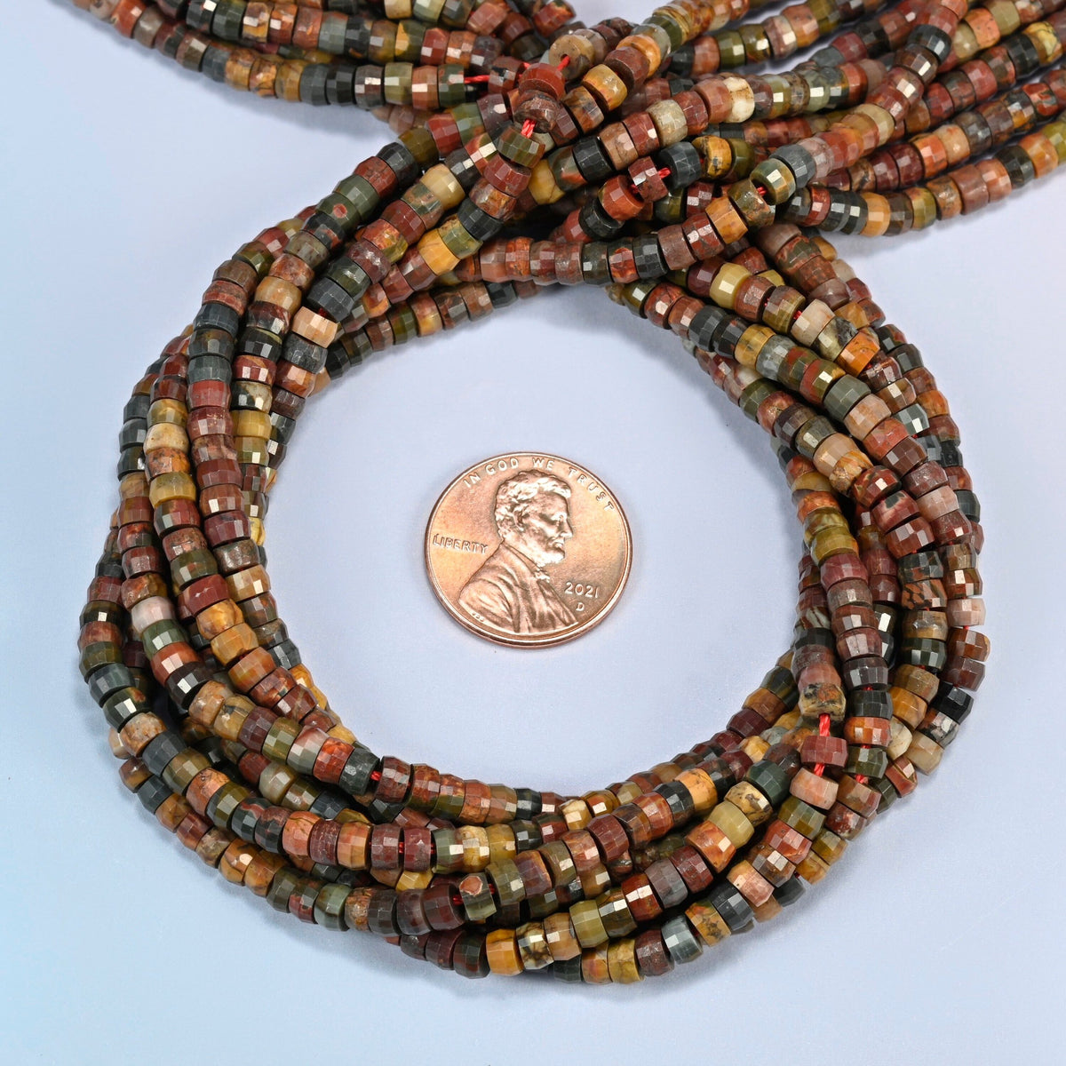 Red howlite faceted heishi disc beads 2x4mm coiled in a loop around a US penny for scale, close-up of the faceted disc shape