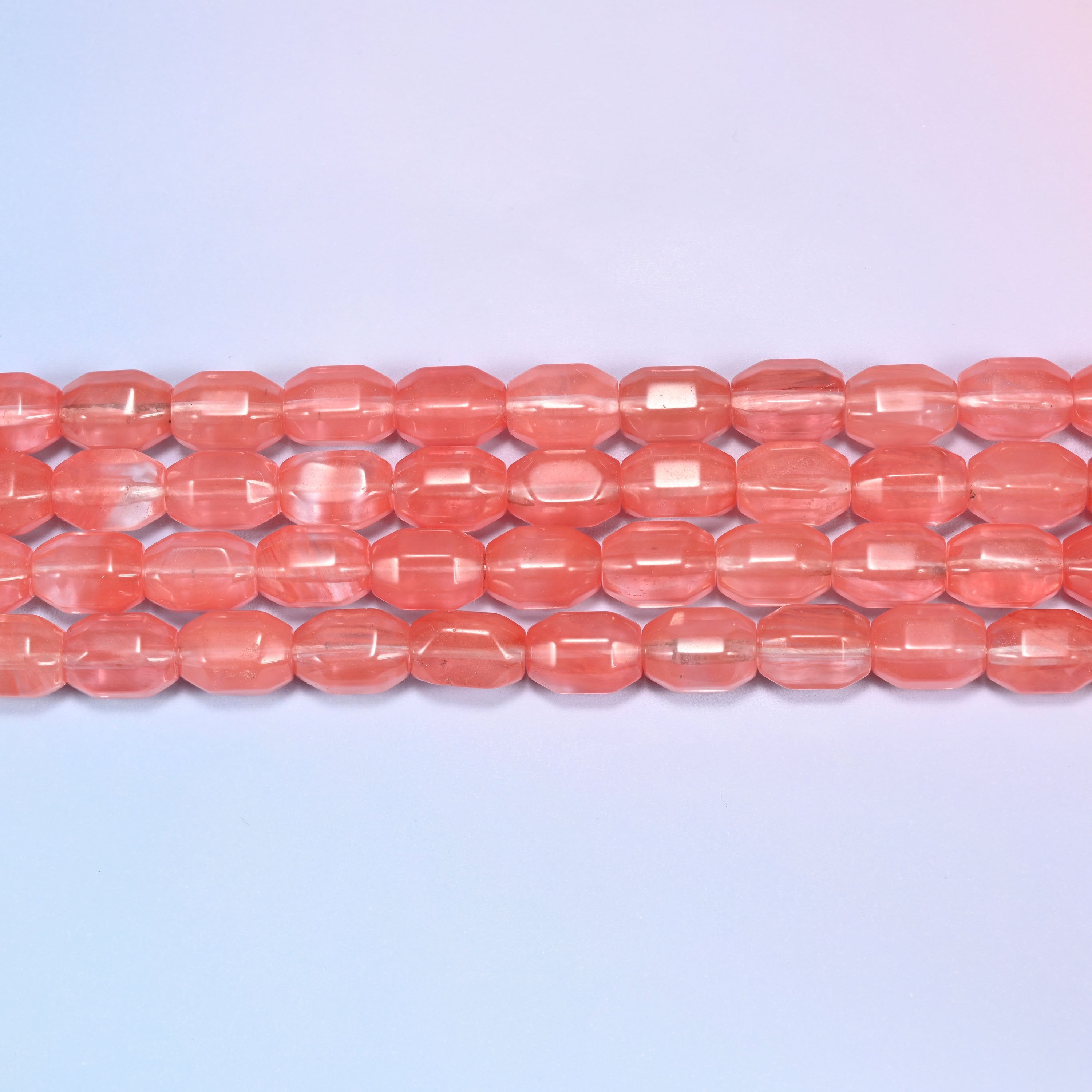 Close-up rows of coral pink faceted glass barrel beads laid flat, showing the translucent glassy finish.