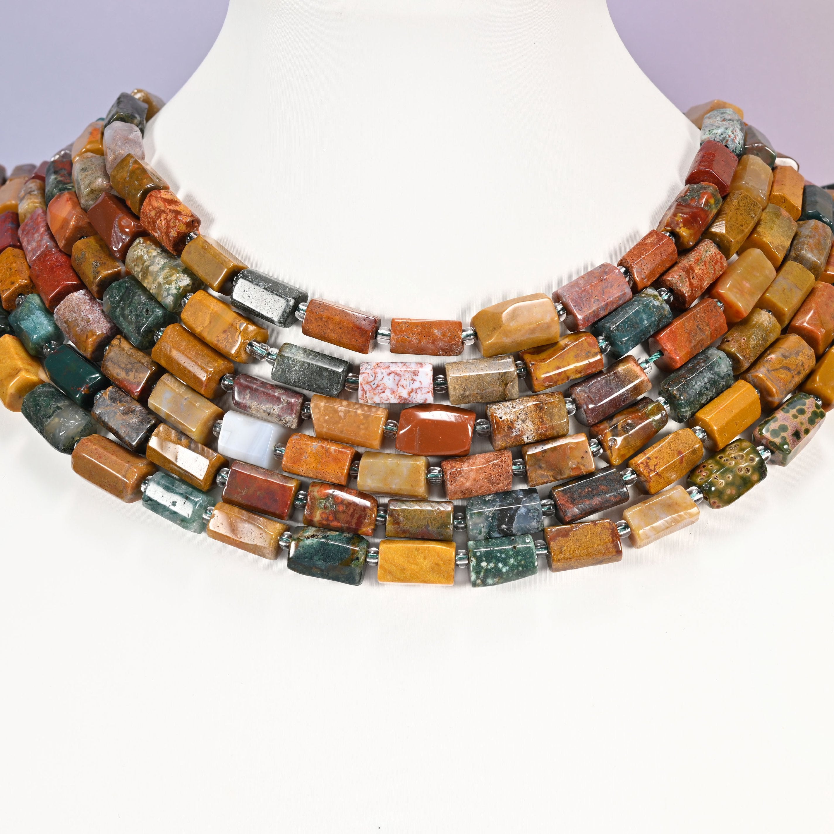 Multi-strand Ocean Jasper faceted tube bead necklace laid flat on a mannequin neck form against a lavender background.