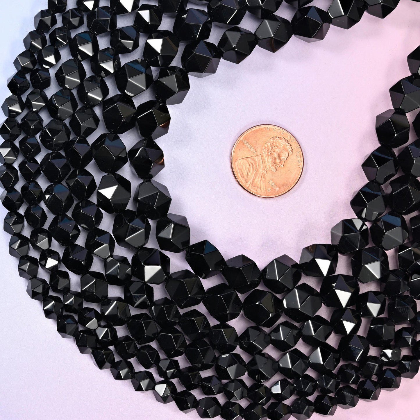 Black Onyx diamond star cut beads coiled around a US penny for size reference, centre drilled