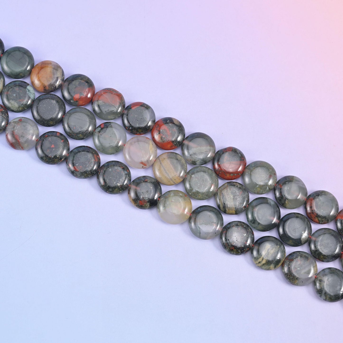 Diagonal run of 15mm African Bloodstone coins on a lilac background