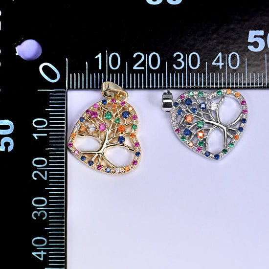 Gold and silver heart tree of life zirconia charms on a black millimetre ruler, shown together for size reference.
