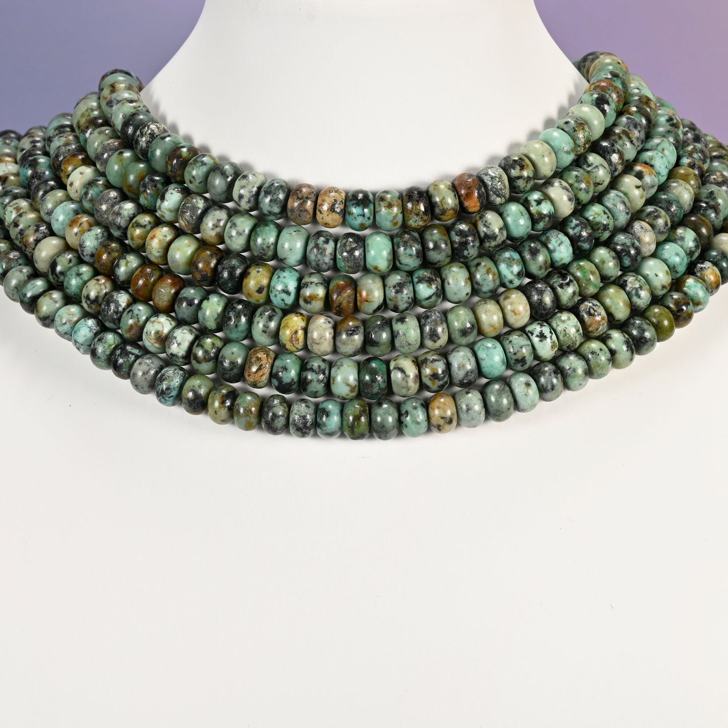 Multi-strand African Howlite necklace laid flat on a mannequin neck form against a lavender background.