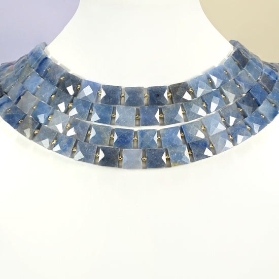 Natural blue aventurine faceted flat square strands arranged as a layered collar on a white display bust, denim blue beads across the neck
