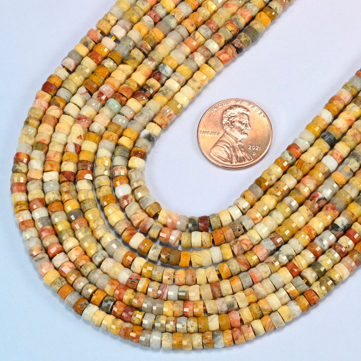 Close view of crazy agate faceted heishi disc strands curving beside a US penny for scale