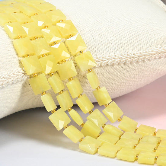 Lemon Jade faceted flat square beads 10x10mm with small gold seed bead spacers, several strands draped over a white cushion