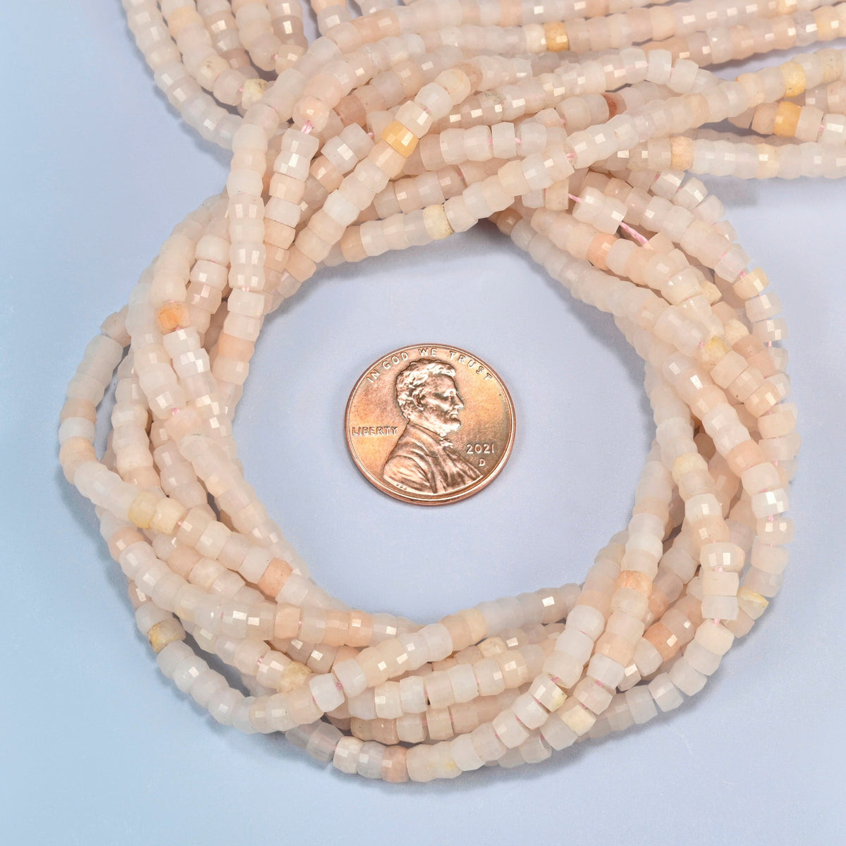 Pink aventurine faceted heishi disc beads 2x4mm coiled in a loop around a US penny for scale, close-up of the faceted disc shape