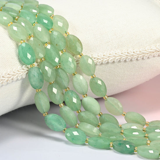 Green aventurine faceted flat oval beads 9x14mm with small gold seed bead spacers, several strands draped over a white cushion