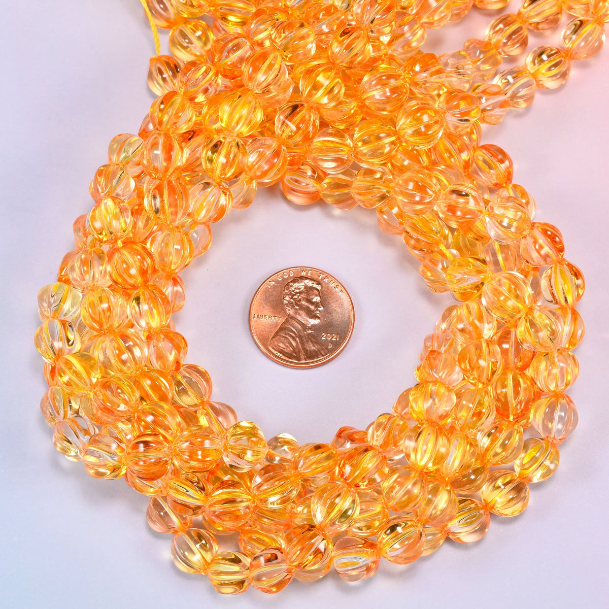A scattered group of loose 8mm yellow gold pumpkin glass beads, showing the melon ribs and the drill holes.