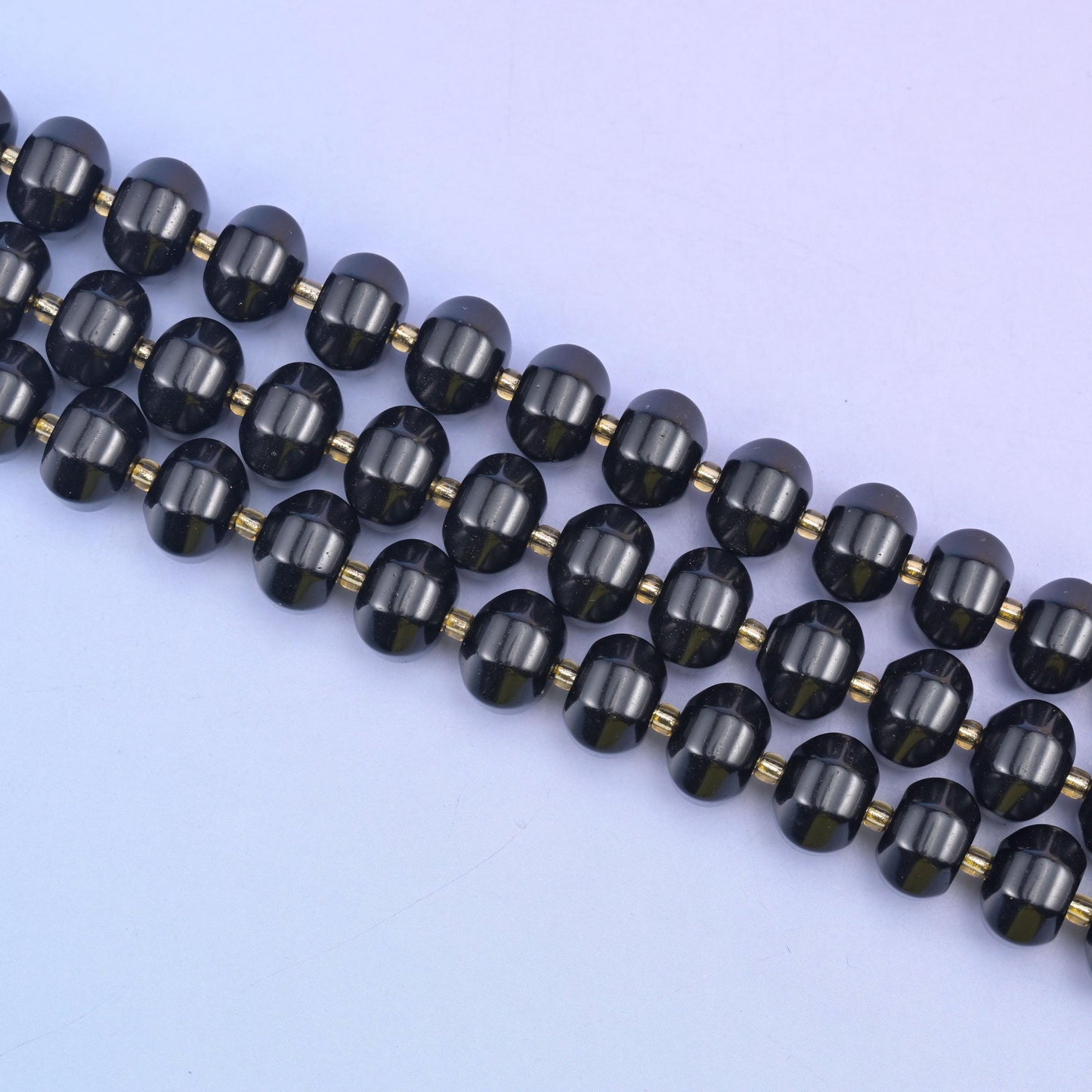 Angled run of 12x8mm obsidian pumpkin rondelles across pale lilac, gold seed beads between each stone