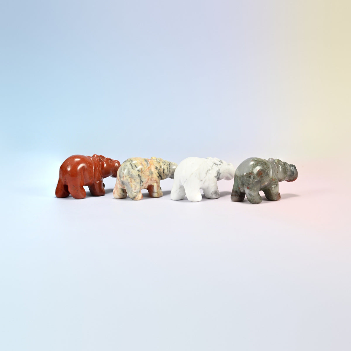 Four small gemstone hippos lined up showing the rounded snout and short legs