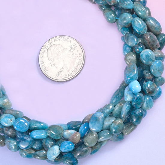 Teal and denim blue tumbled into smooth freeform pebbles, semi-translucent in places and streaked with grey-green and darker slate, so the strand looks like a handful of sea-worn stones.