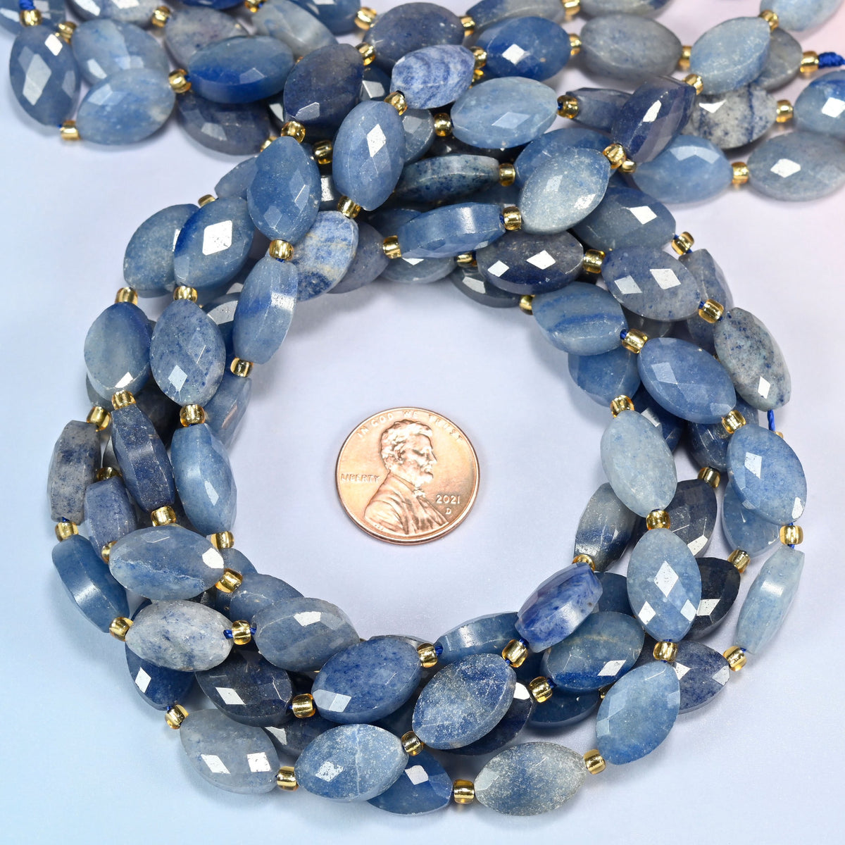 Blue aventurine faceted flat oval beads 9x14mm coiled in a loop around a US penny for scale, close-up of the faceted flat oval shape