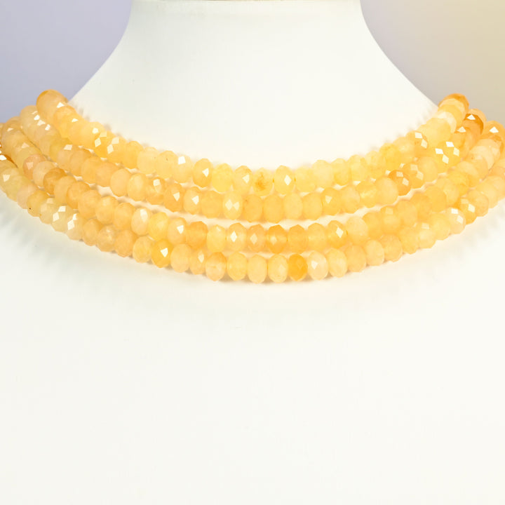Yellow jade faceted rondelle strands arranged as a layered collar on a white display bust, butter yellow beads across the neck
