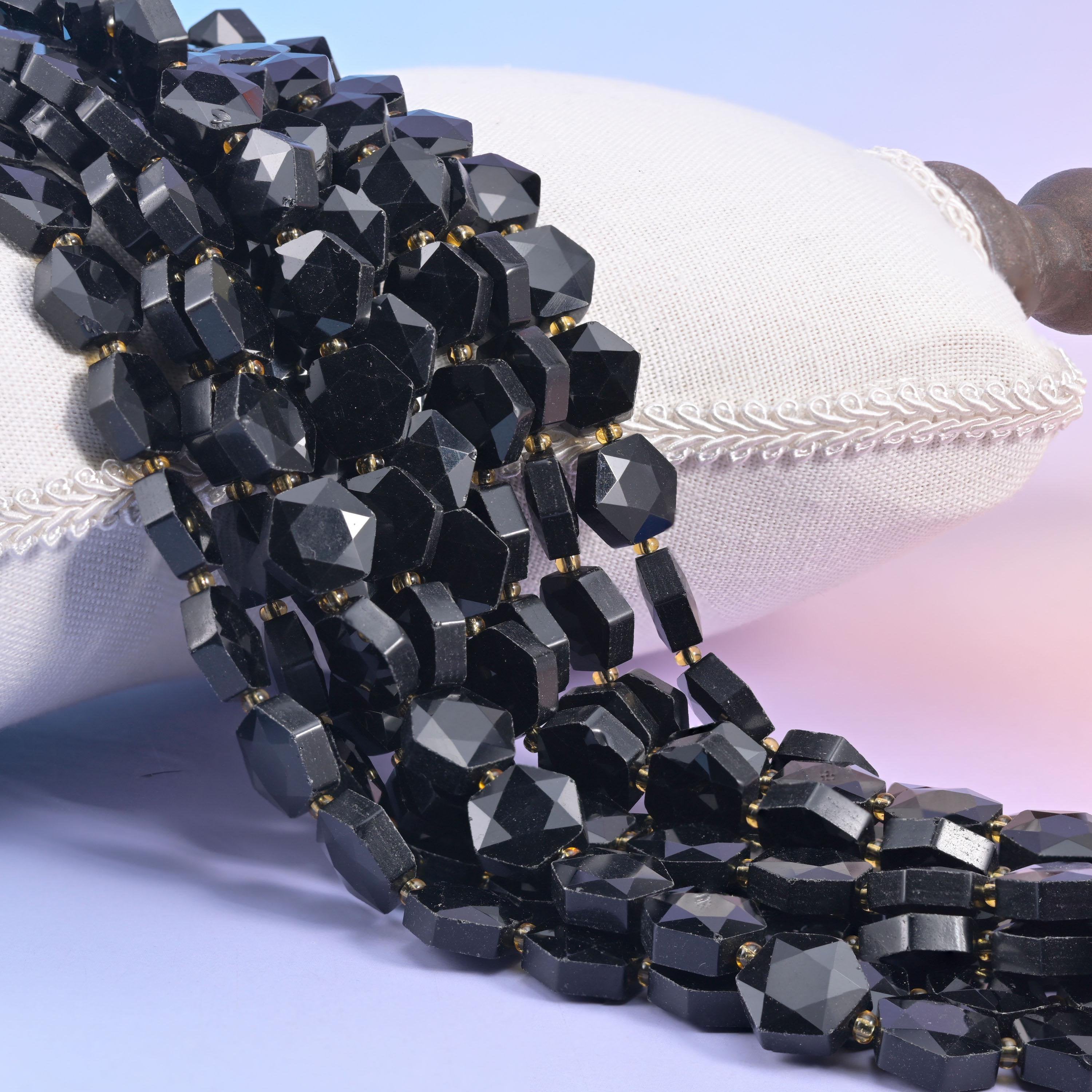 Black obsidian hexagon strands draped over a white cushion, faceted faces flashing silver where the light hits