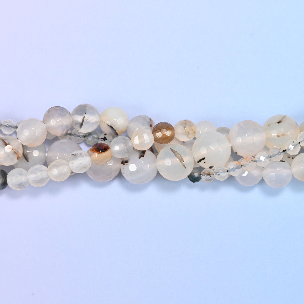 Milky white and cloudy cream rounds, semi translucent, scattered with dark brown and black dendritic flecks and the occasional amber patch. Faceted all over