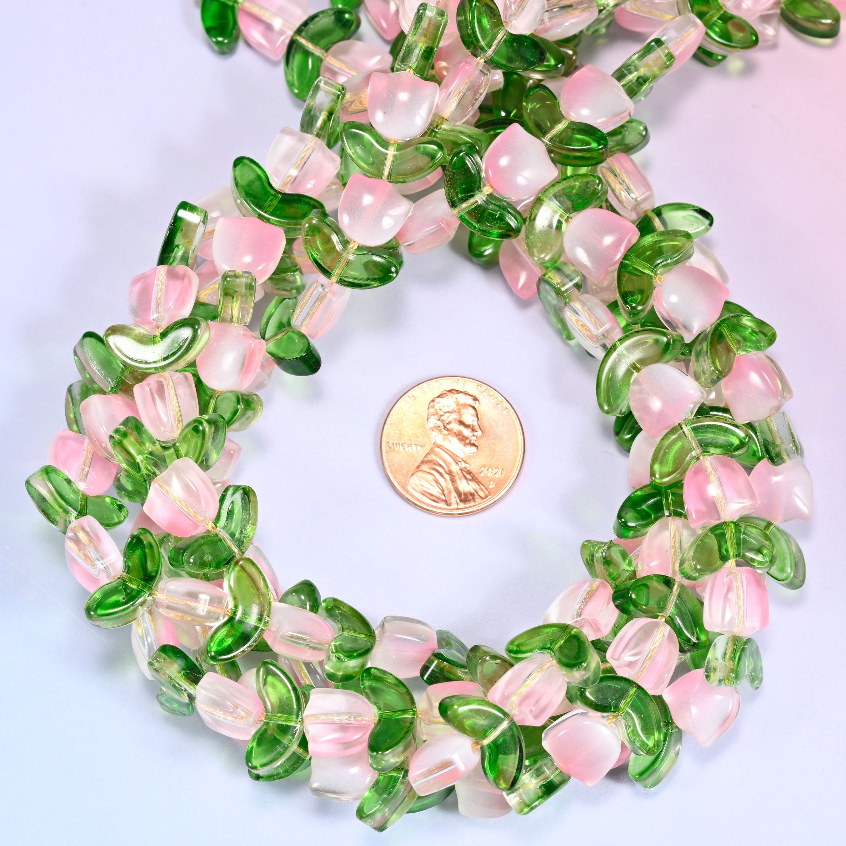 Close-up circular coil of tulip and leaf glass bead strands on a lavender background with a penny in the center for size comparison.