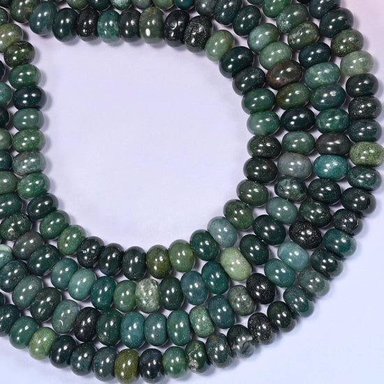 Rows of Moss Agate rondelle beads laid straight on a lavender surface, showing the natural stone color variation.