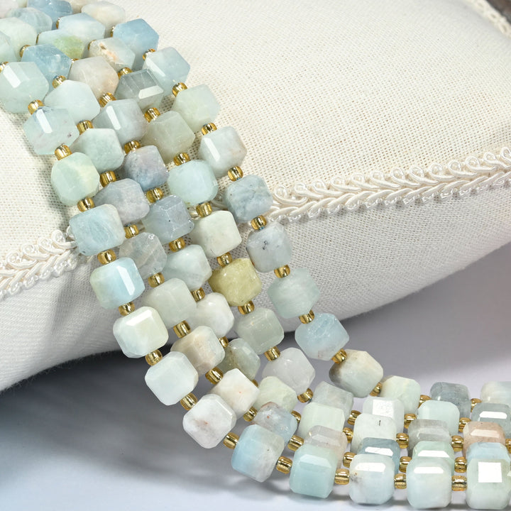 Aquamarine faceted cube beads draped over a white cushion, soft blue and cream cubes with gold spacers.