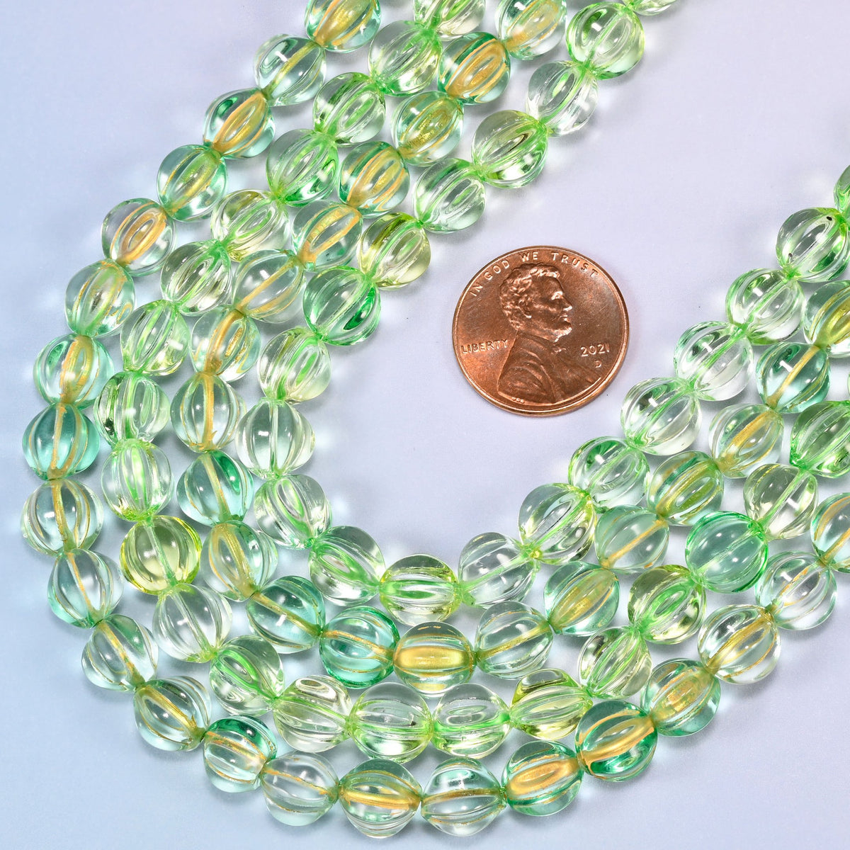 Green gold pumpkin glass beads coiled loosely, shown with a US penny resting on the strands for scale.