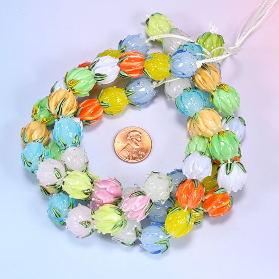Loose bundled coil of tulip bud lampwork glass bead strands with visible stringing cord ends, on a lavender background, with a penny in the center for size comparison.