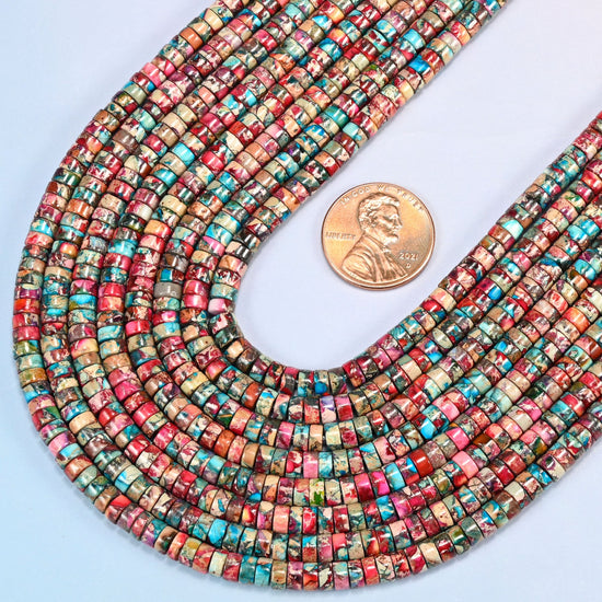 Close view of dyed pink blue sea sediment jasper heishi disc strands curving beside a US penny for scale
