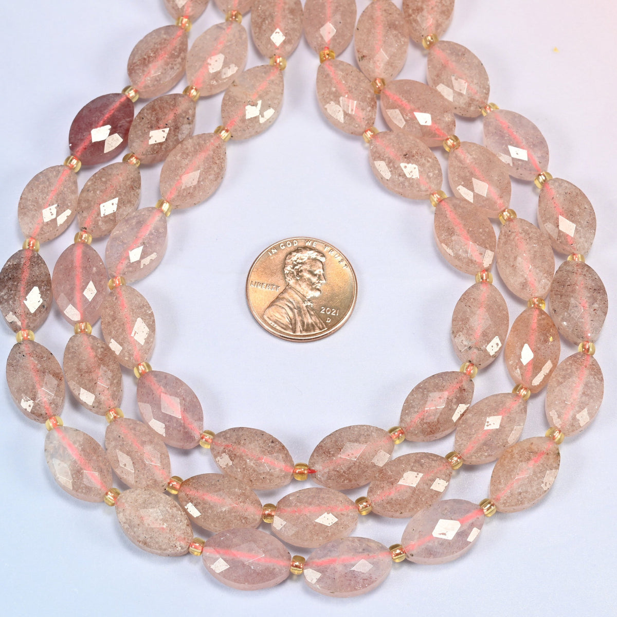 Strawberry quartz faceted flat oval strands formed into a teardrop loop around a US penny for scale