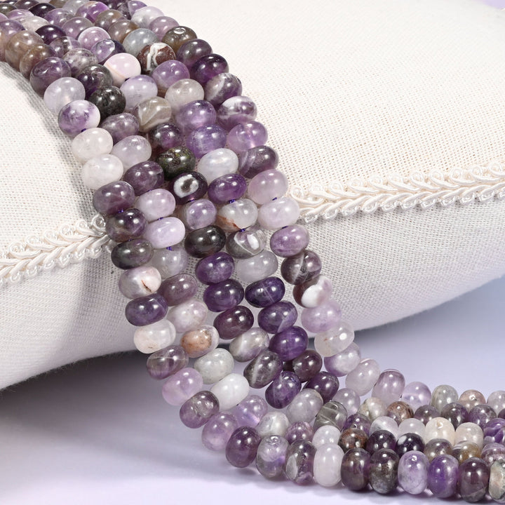 Close-up of multiple strands of polished Amethyst rondelle beads in purple and smoky tones, draped over a cream fabric jewelry display bust.