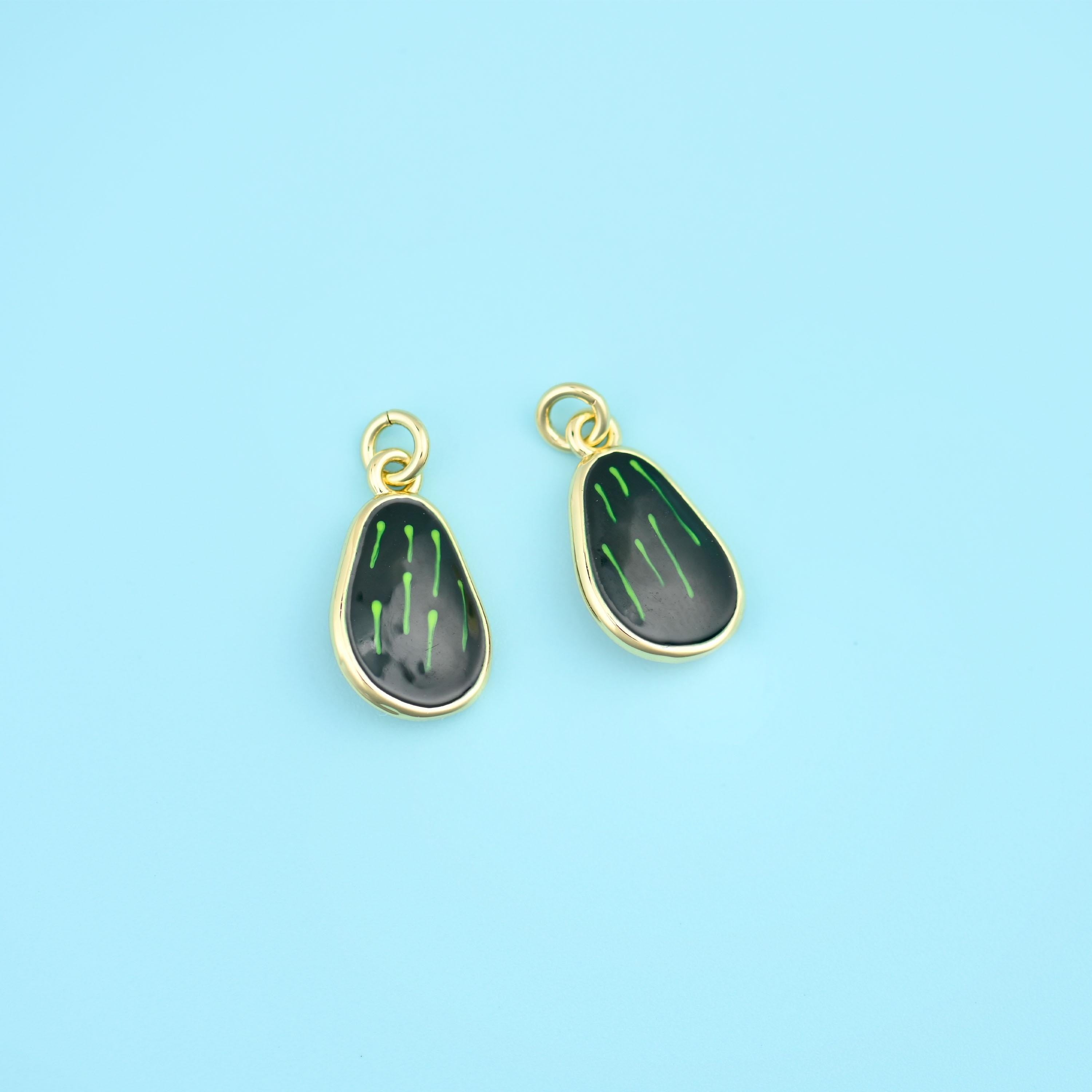 A little glossy avocado half with a domed burgundy stone set where the pit sits, the enamel body outlined in a bright gold…