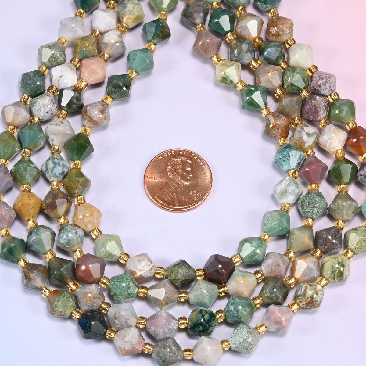 Indian Agate faceted bicone beads 8mm with gold-tone spacers, strand coiled into a neat circle with a penny centered for scale