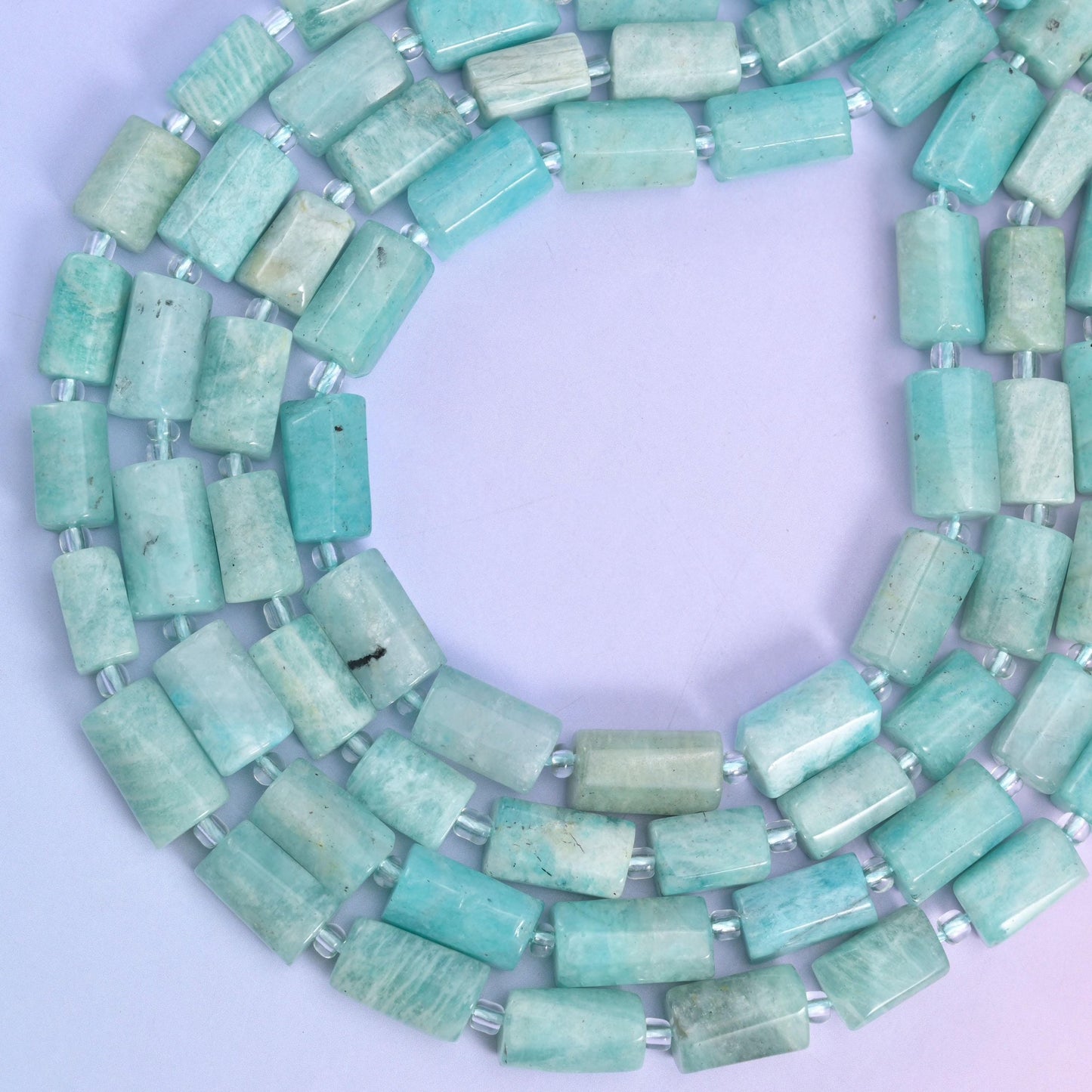Strands coiled into a ring on a pink-lilac backdrop, showing the full 15.5 inch strand length