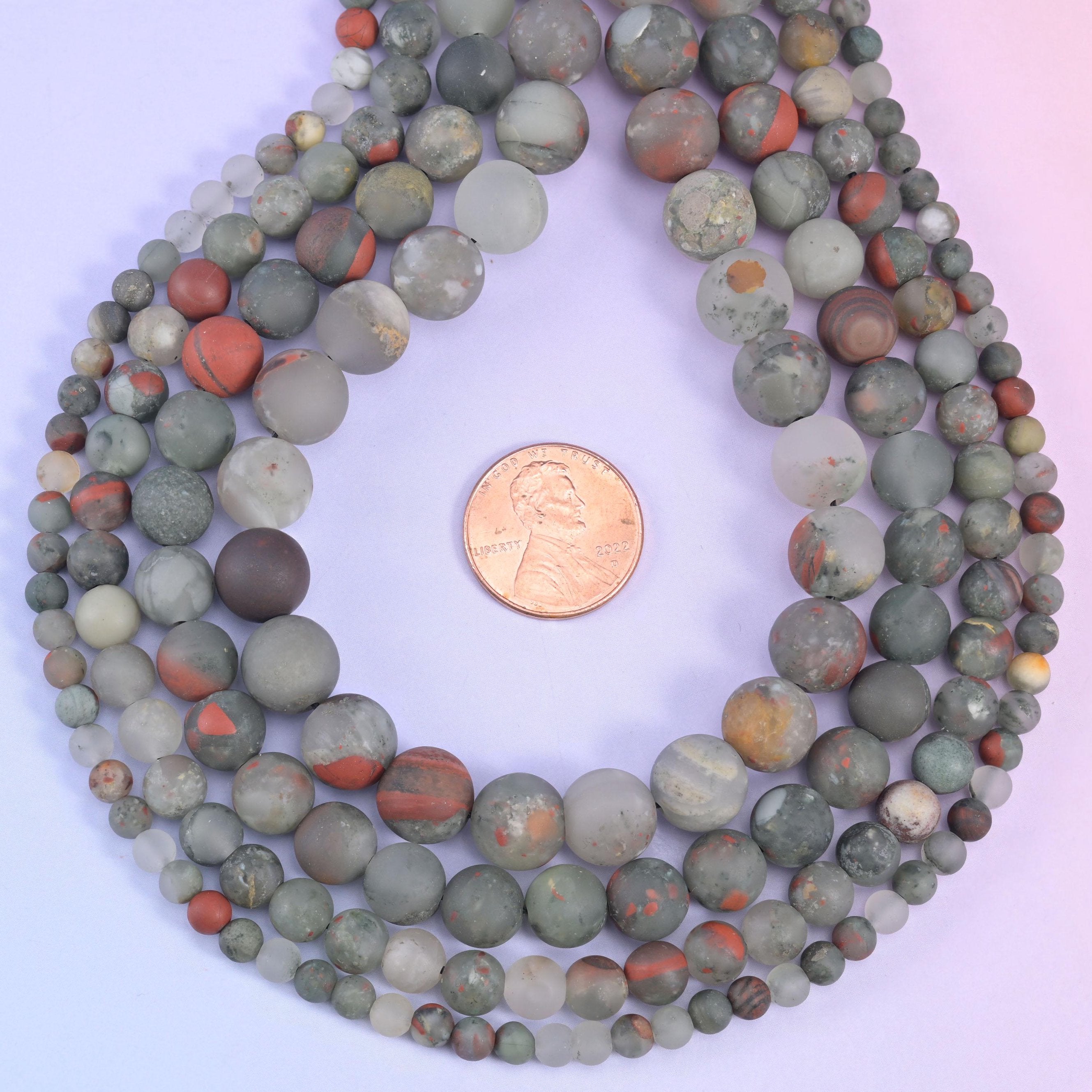 Muted sage and grey-green rounds shot through with brick and rust red — some beads almost entirely terracotta, others cool stone grey flecked with cream