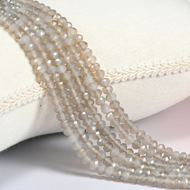 Gray Agate faceted rondelle beads draped over a cream fabric cushion, soft gray and light gray with milky white banding across the 4x6mm strands.