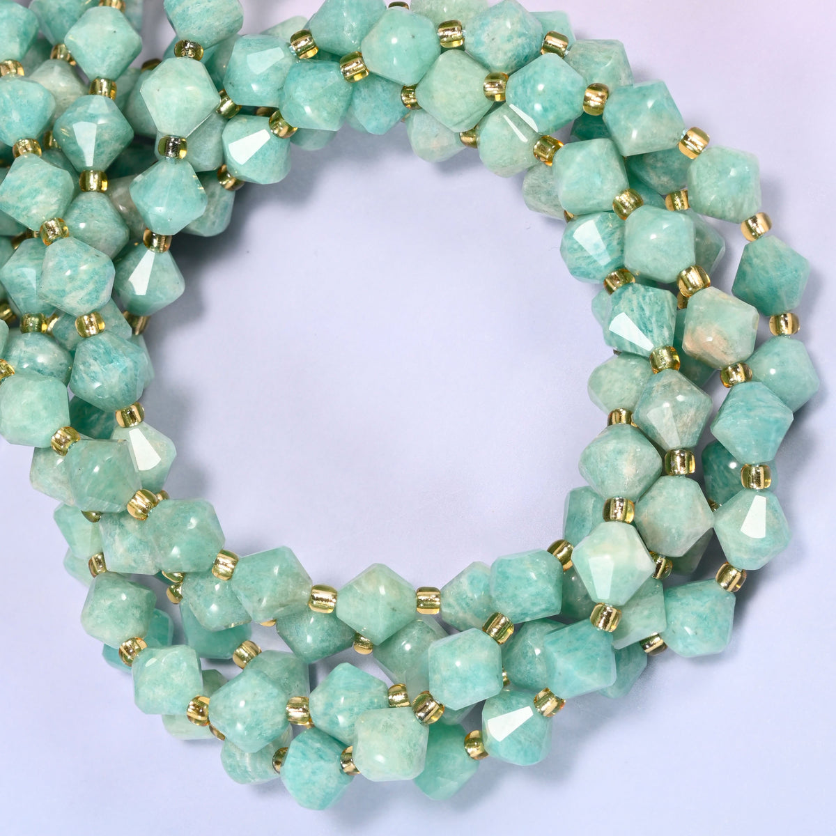 Green Amazonite faceted bicone beads 8mm with gold-tone spacers, strand coiled into a tighter circle, close-up view