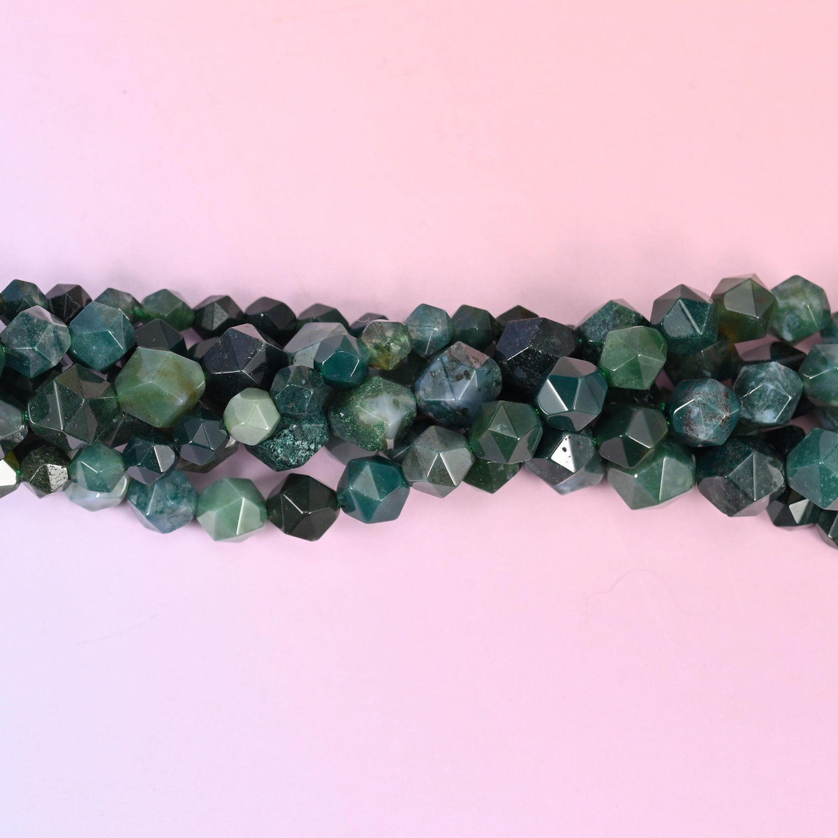 Moss Agate faceted beads close up in a single row, flat triangular star cut planes over mossy green dendritic patterning