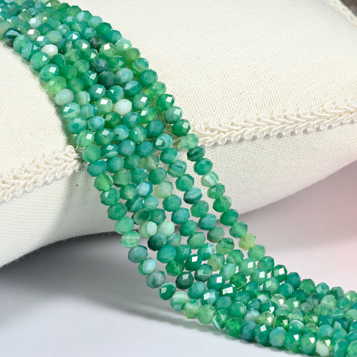 Dyed Green Strip Agate gemstone rondelle beads 4x6mm faceted, strand draped over a cream fabric cushion