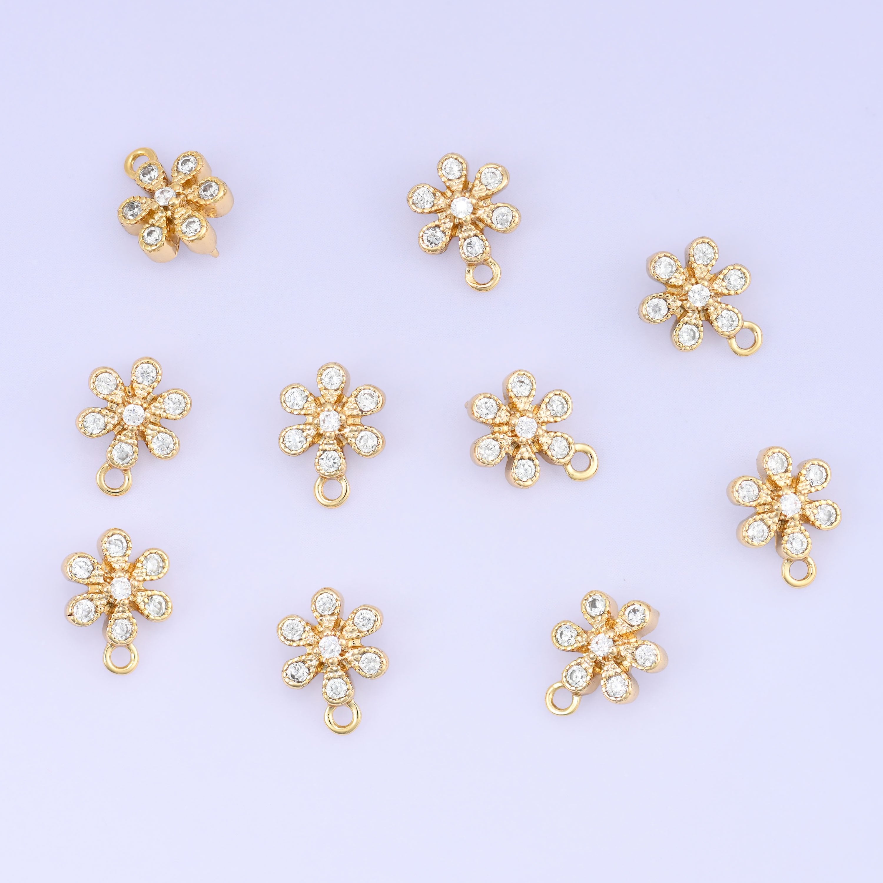 Small gold charms, eleven gold plated flower charms with clear cubic zirconia scattered on a pale backdrop