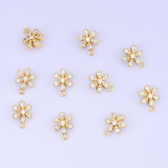 Small gold charms, eleven gold plated flower charms with clear cubic zirconia scattered on a pale backdrop
