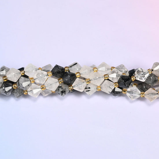 Black rutilated quartz bicone beads shown as a single strand laid straight across, the black needle inclusions running at different angles in every bead.