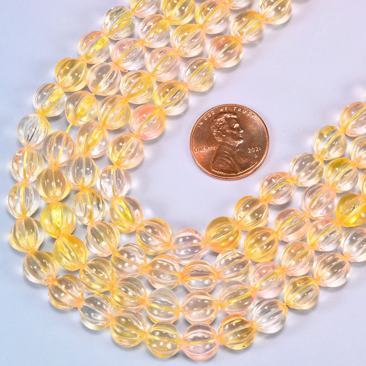 Yellow clear pumpkin glass beads coiled loosely, shown with a US penny resting on the strands for scale.