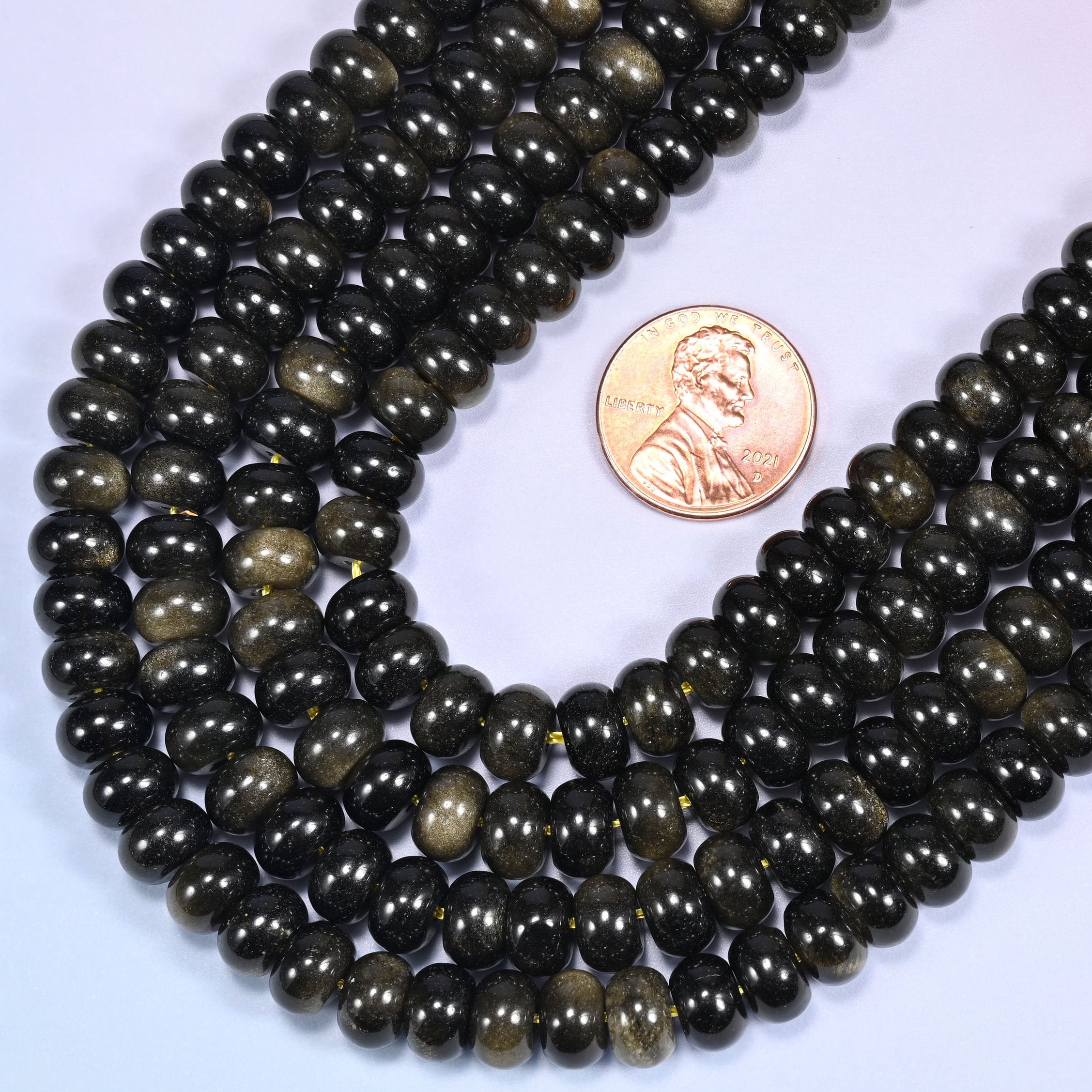 Rows of Gold Obsidian rondelle beads laid straight on a lavender surface, showing the golden sheen variation.