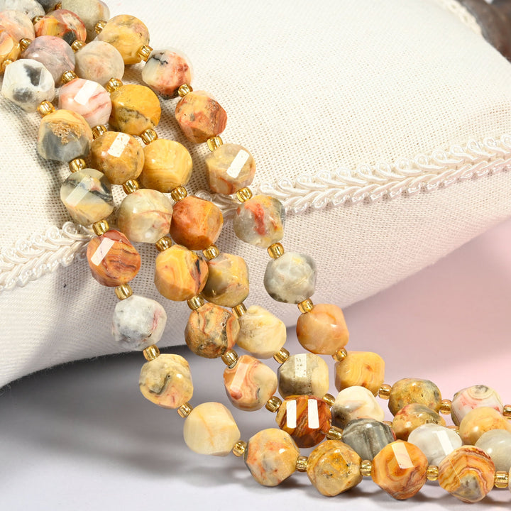 Crazy agate faceted spiral twist beads against a white cushion, yellow and gray stone with red swirls.