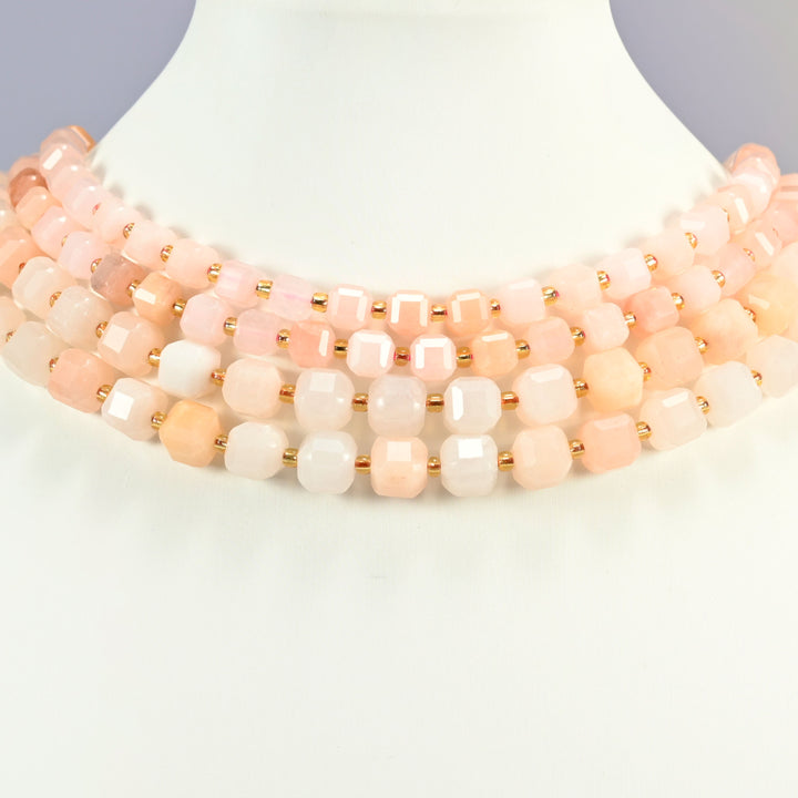 Pink aventurine faceted cube strands arranged as a layered collar on a white display bust, peach, blush and cream beads across the neck