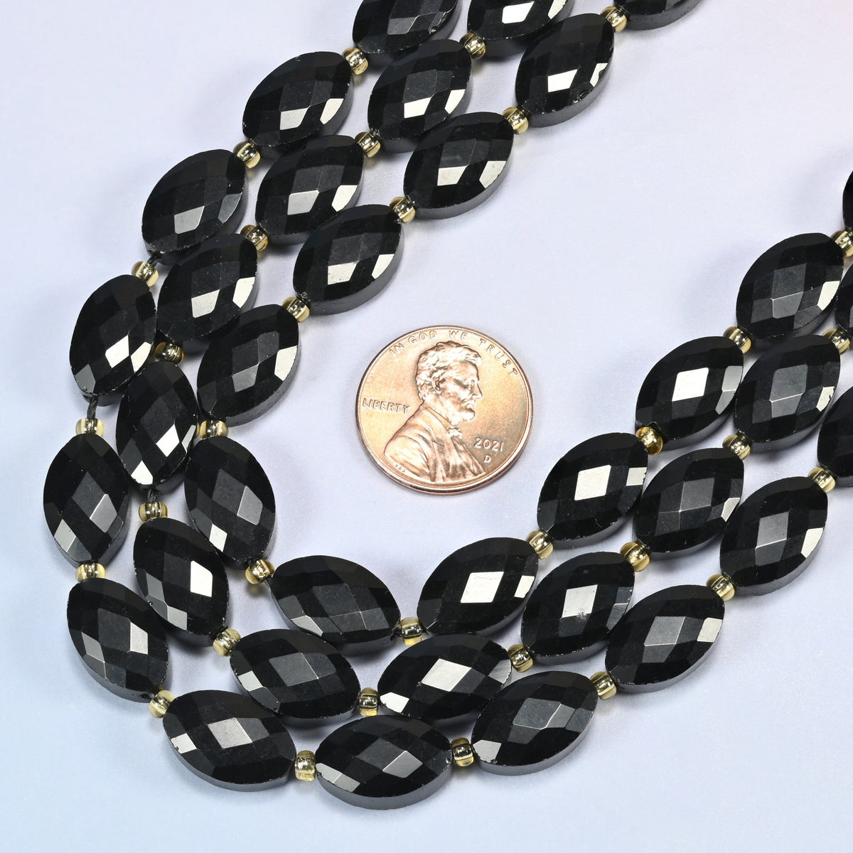 Close view of black onyx faceted flat oval strands curving beside a US penny for scale