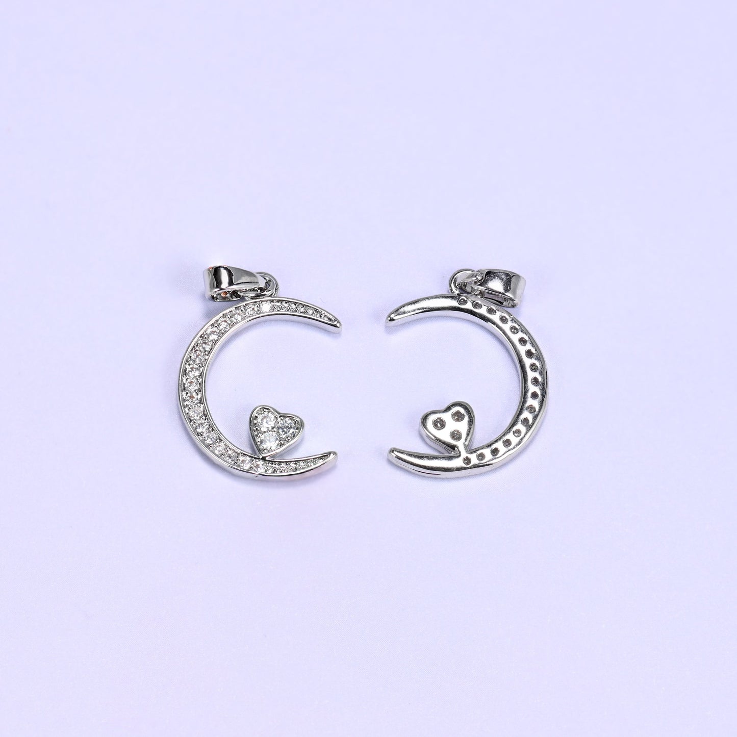 Silver-tone moon heart zirconia charm beside one turned over, showing the paved crescent and its smooth back together.
