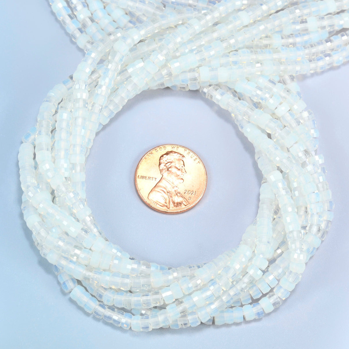 Opalite faceted heishi disc beads 2x4mm coiled in a loop around a US penny for scale, close-up of the faceted disc shape