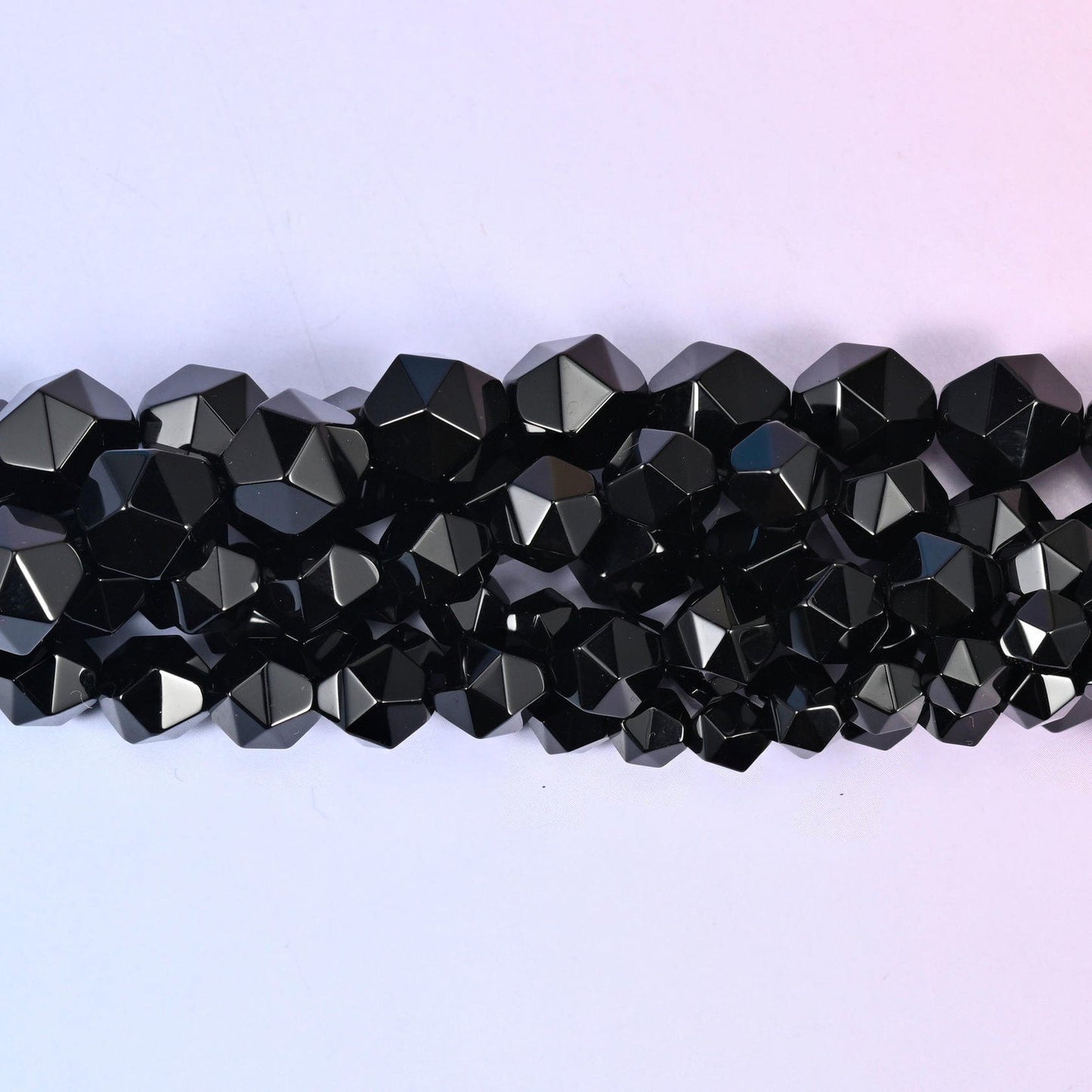 Black Onyx faceted beads close up in a single row, flat triangular star cut planes on a glossy black finish