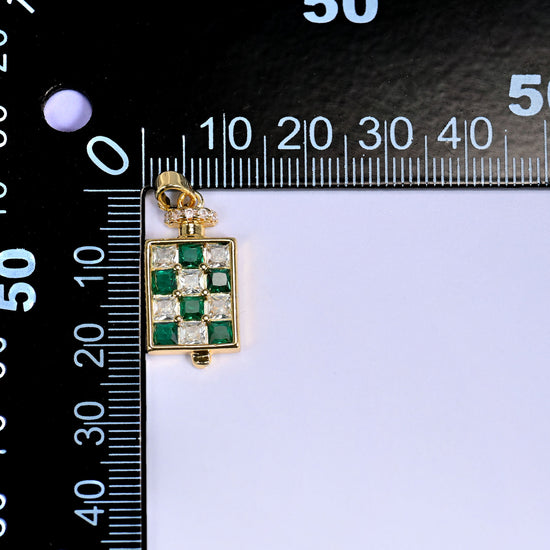 Perfume bottle zirconia charm against a black millimetre ruler, the green pendant lined up at the zero mark for size reference.